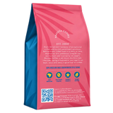A standing bag of Brazuca Coffee single-origin roasted coffee beans, featuring a vibrant pink and blue gradient design with white text and circular icons indicating key attributes.
