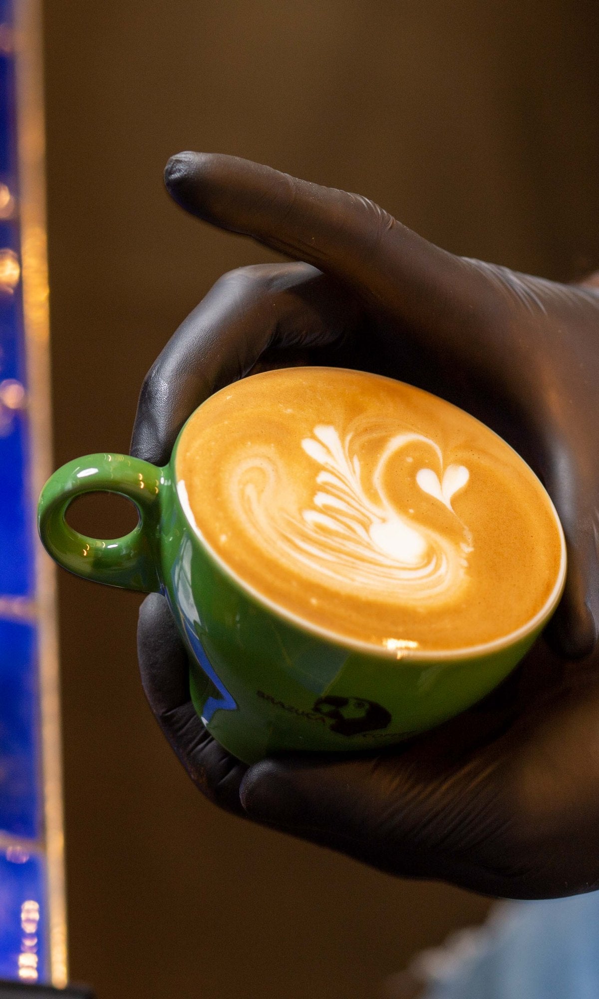 Barista holding a cappuccino with latte art in a green Brazuca cup