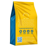 A standing bag of Brazuca Coffee Roasters single origin coffee beans, showing the back panel with a bright yellow and blue design, text, icons, and a QR code on a white background.