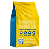 A standing bag of Brazuca Coffee Roasters single origin coffee beans, showing the back panel with a bright yellow and blue design, text, icons, and a QR code on a white background.